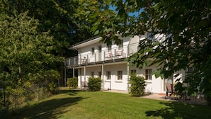 A two-story building with a balcony, surrounded by greenery and trees. - Vacation apartment WE10 - Holiday apartments at the sports field (Sellin)