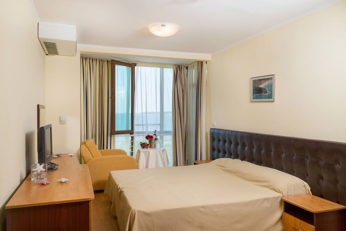 A hotel room with a bed, a desk, a television, and a window with curtains.