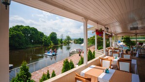A covered outdoor dining area with tables and chairs, overlooking a river with boats and greenery. - Perla Sun Park Hotel (Primorsko)