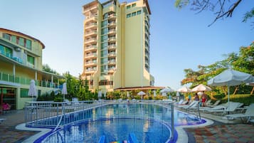 A swimming pool with a rainbow slide, surrounded by lounge chairs and umbrellas, with a tall building in the background.