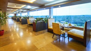 A modern hotel lobby with seating areas, large windows, and a city view. - Kpm Tripenta Hotel (Kozhikode)