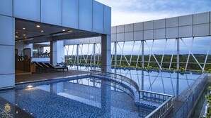 A modern hotel with a rooftop infinity pool, outdoor seating, and a view of the cityscape. - Kpm Tripenta Hotel (Kozhikode)