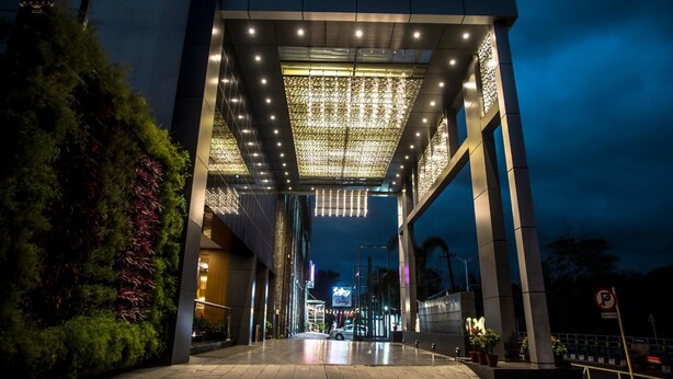 A modern building entrance with a covered walkway, illuminated by overhead lights, and surrounded by greenery. - Kpm Tripenta Hotel (Kozhikode)