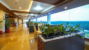 A spacious lobby with a high ceiling, large windows, and a reception desk with plants. - Kpm Tripenta Hotel (Kozhikode)