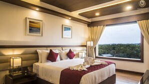 A hotel room with a large bed, two bedside tables, a nightstand, a window with curtains, and framed artwork on the wall. - Kpm Tripenta Hotel (Kozhikode)