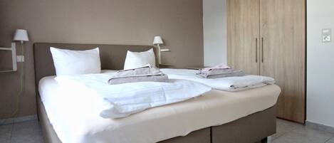 Una habitación de hotel moderna con una cama grande, dos mesitas de noche, un armario y una lámpara de pared.