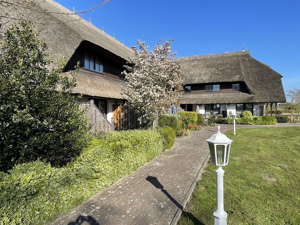 Un bâtiment traditionnel à toit de chaume, accessible par un chemin pavé, et entouré de verdure.