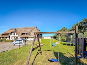 Une maison avec un toit de chaume, une balançoire et une voiture garée dans l’allée.