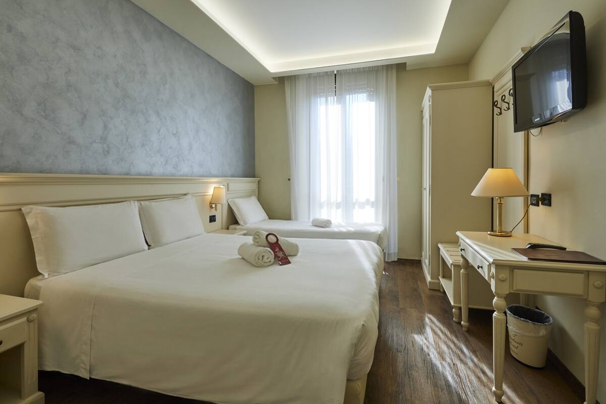 A hotel room with a large bed, a desk, a TV, and a window with curtains.