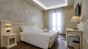 Une chambre d’hôtel bien rangée, avec un grand lit, des lampes de chevet, une petite table et une poubelle.