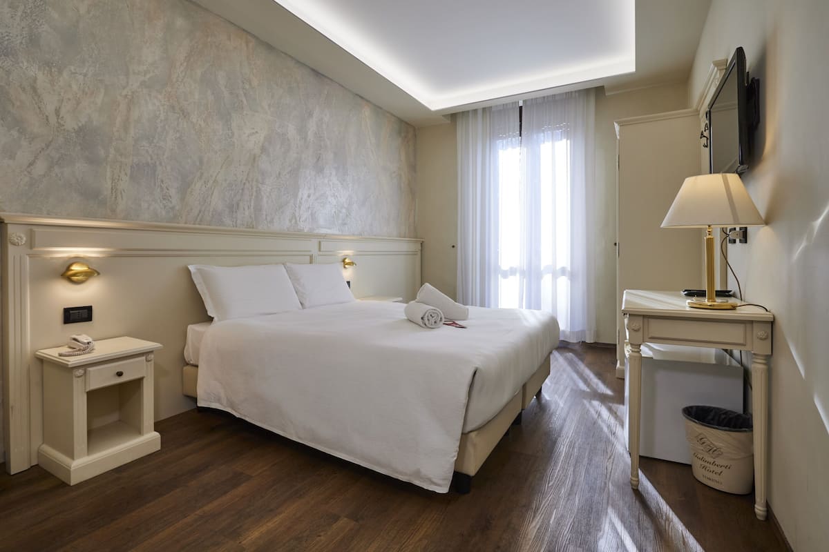 A neatly arranged hotel room with a large bed, bedside lamps, a small table, and a trash bin.