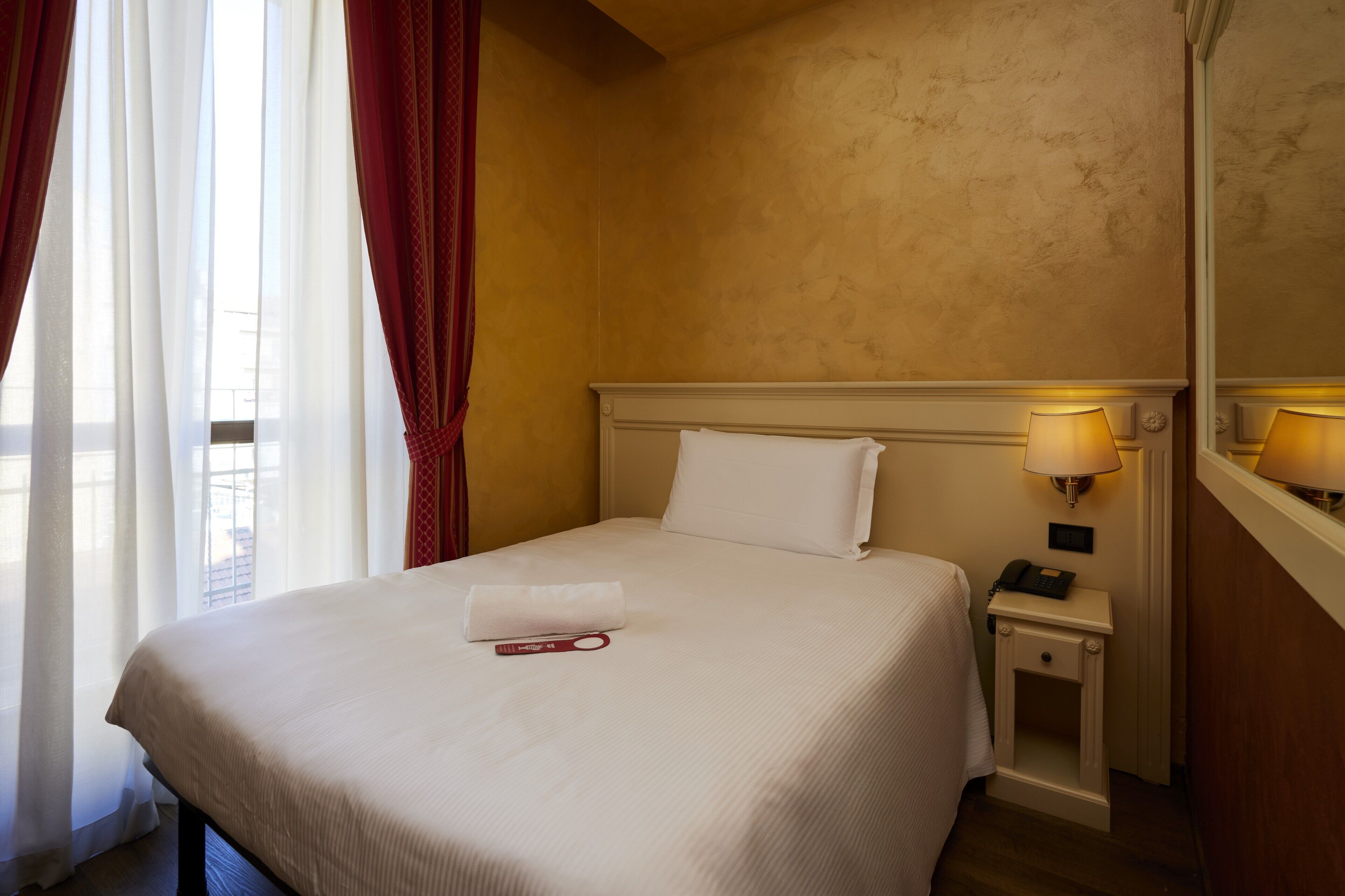 A hotel room with a neatly made bed, a bedside lamp, and a telephone on the nightstand.