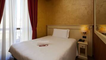 A hotel room with a neatly made bed, a bedside lamp, and a telephone on the nightstand.