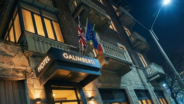 L’entrée d’un hôtel, avec une enseigne indiquant « HÔTEL GALIMBERTI » et des drapeaux.