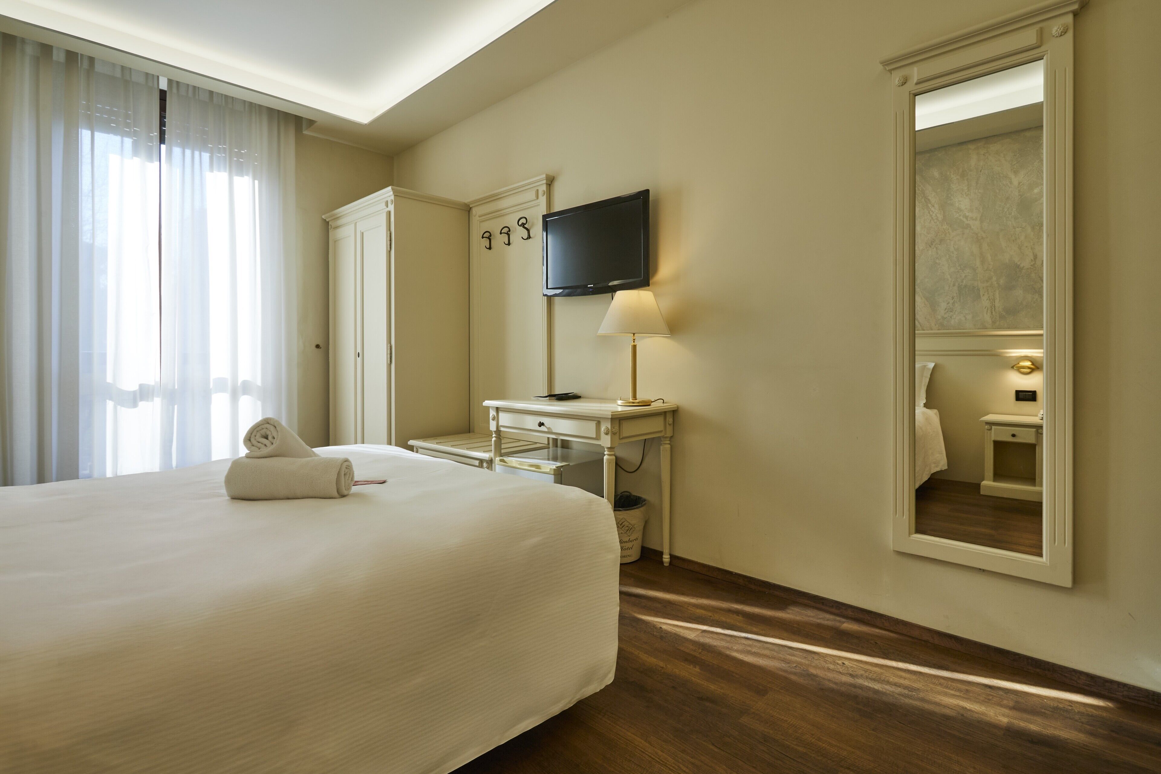 Una habitación de hotel con una cama grande, un escritorio, una televisión, un espejo y una ventana con cortinas.