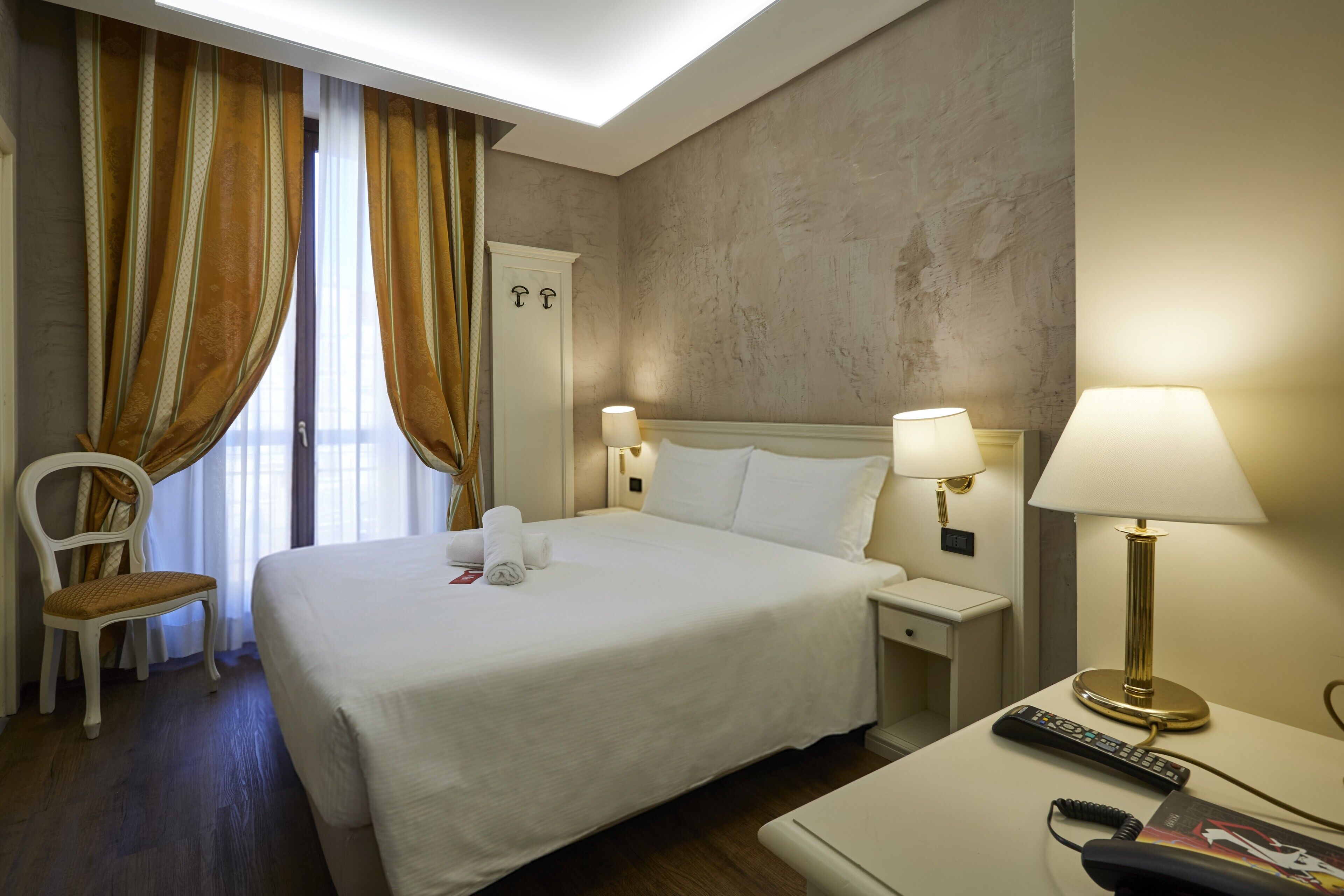 Ein Hotelzimmer mit Bett, Stuhl, Nachttisch, Lampe und Fernbedienung.