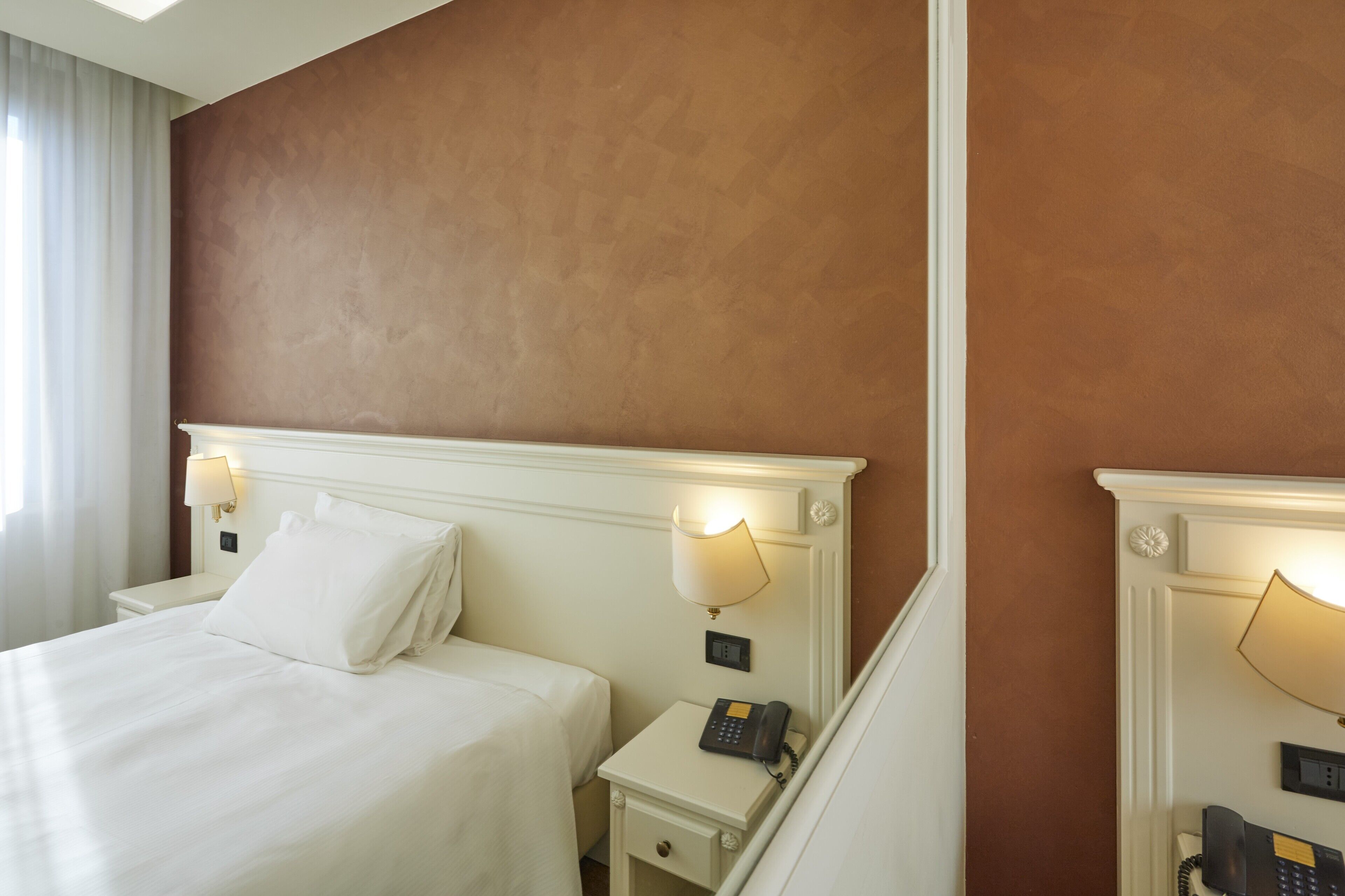 Ett hotellrum med en stor säng, två sängbord med lampor och en telefon på ett av borden.