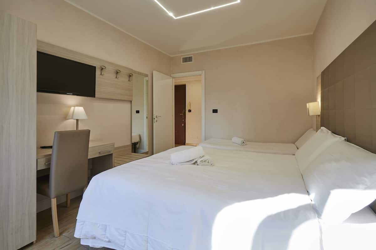 A hotel room with a bed, desk, chair, TV, and a door leading to another room.