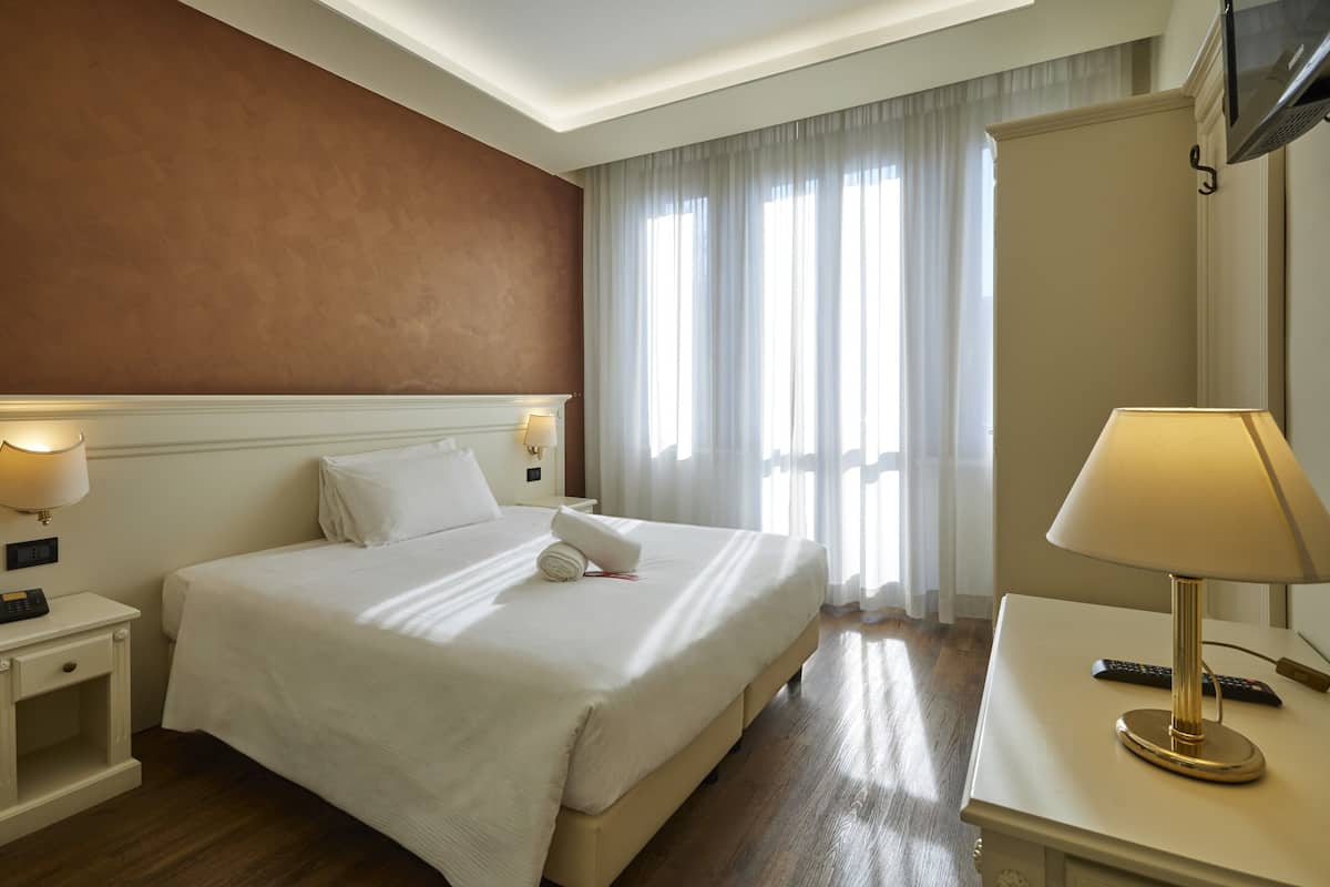 A hotel room with a large bed, bedside lamps, a desk with a lamp, and a television mounted on the wall.