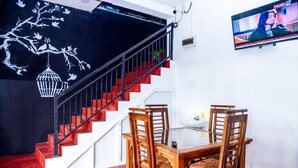 A staircase with red steps and a black wall with white tree and bird decorations. There is a TV on the wall and a table with chairs in the foreground. - Nature Life Guest Inn (Ella)