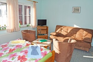 Een slaapkamer met een bed, een bruine bank, een televisie op een houten standaard en een raam met gordijnen.