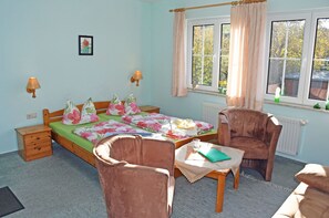 Ein Schlafzimmer mit einem Bett, zwei Stühlen, einem Tisch, einem Nachttisch und einem Fenster mit Vorhängen.