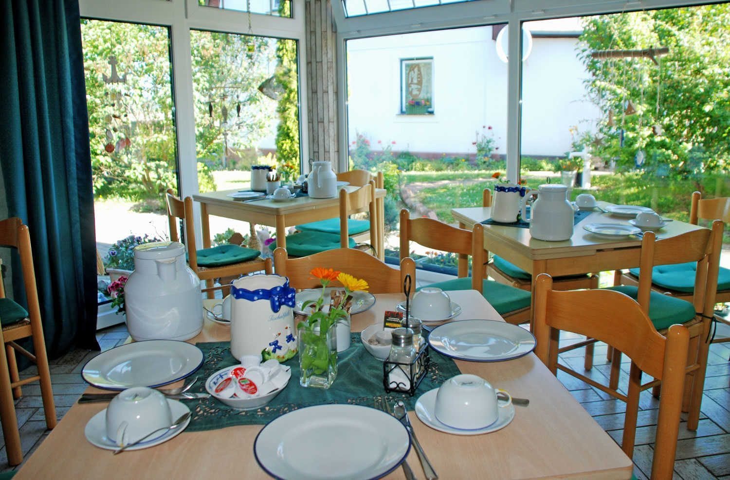 A dining area with tables set for breakfast, featuring white plates, cups, and a pitcher.