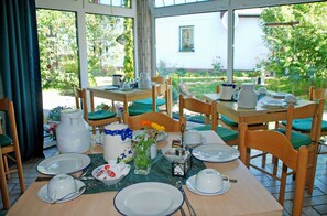 Ein Essbereich mit gedeckten Tischen für das Frühstück, mit weißen Tellern, Tassen und einer Kanne.