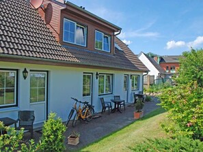 A two-story house with a tiled roof, a patio with outdoor furniture, and a bicycle parked outside.