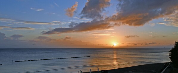 A sunset over a calm sea with a pier extending into the water.