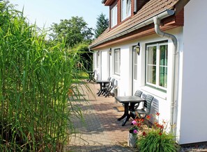 Een terras met een tafel en stoelen, omringd door groen en een wit gebouw met ramen.