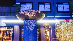 Een gebouw met een grote decoratieve kolom ervoor, grote ramen en een goed verlicht interieur.