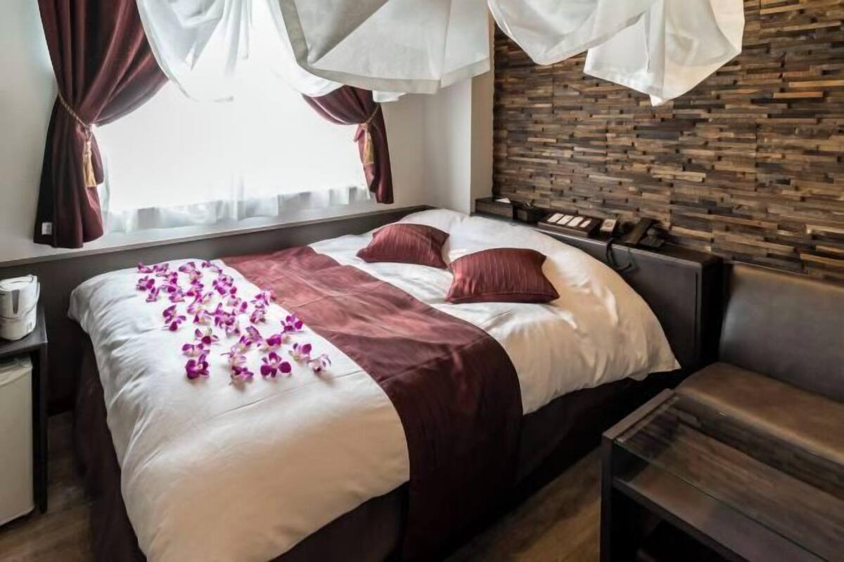 Ett hotellrum med en säng, ett sängbord, ett litet bord vid sängen, en träpanel som huvudgavel och en vägg med ett mönster som efterliknar tegelstenar.