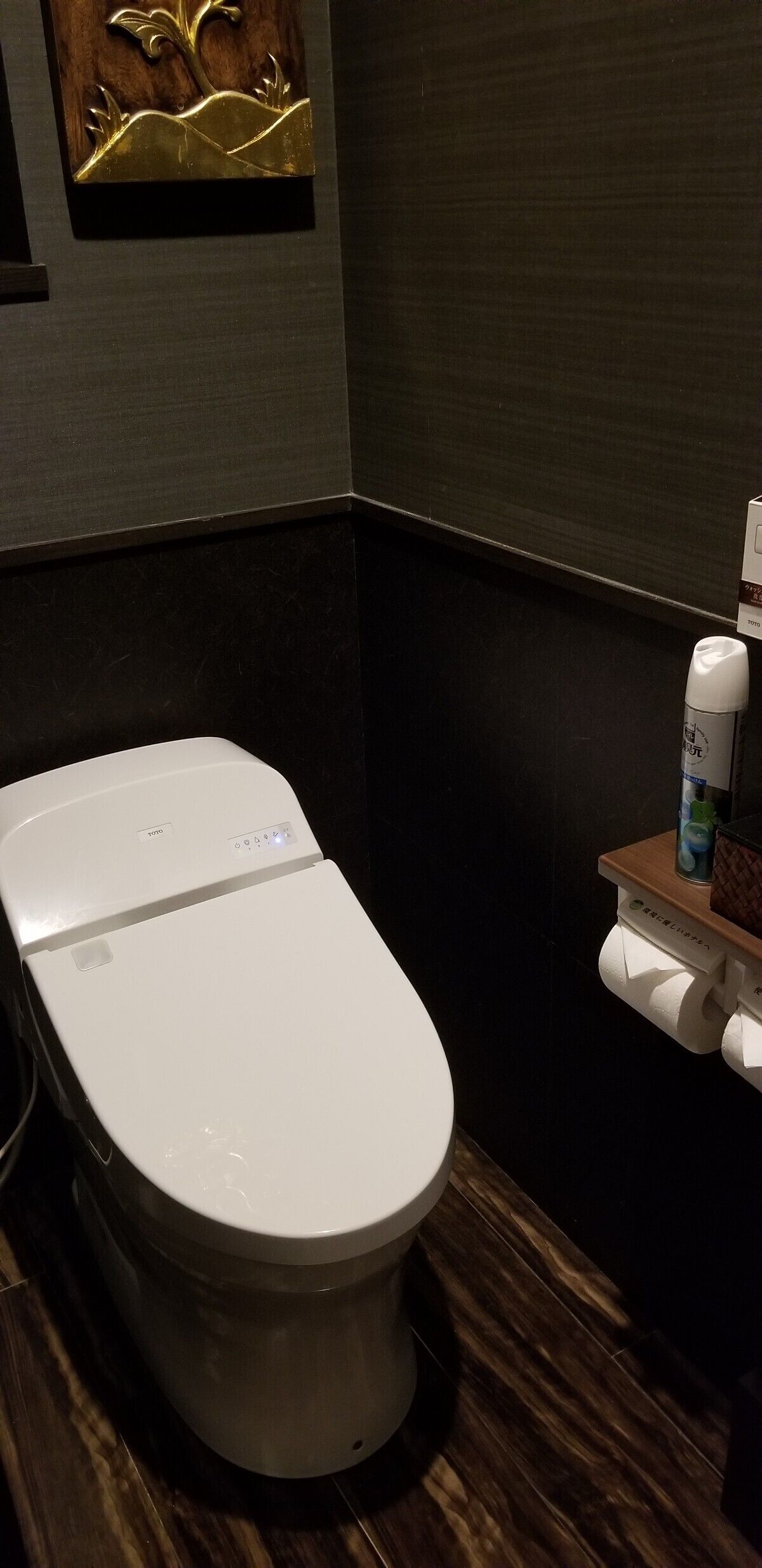 Une salle de bain moderne avec des toilettes blanches, un plancher en bois et un porte-rouleau de papier toilette fixé au mur.