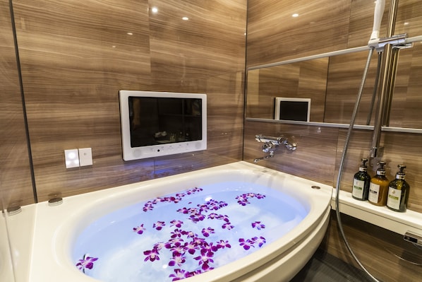 Un baño moderno con una bañera grande, un cabezal de ducha de mano y un televisor montado.