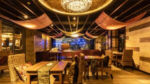 Een restaurant met rieten meubels, houten tafels en een centrale zithoek.