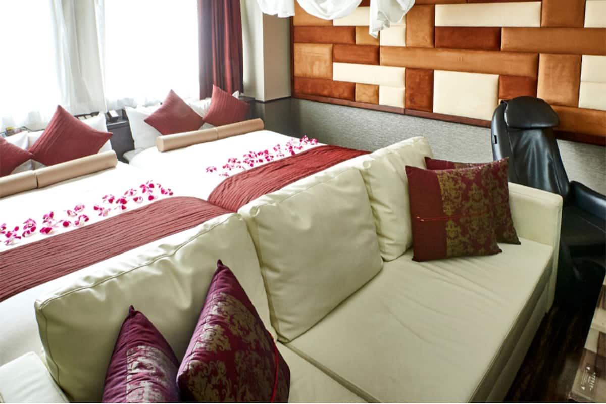 Ett hotellrum med två sängar, en soffa och en sänggavel med en träpaneldesign.