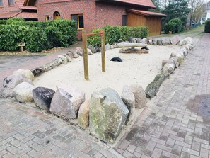 Zona de juegos arenosa con rocas grandes y un conjunto de columpios de madera.