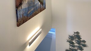 Een schilderij aan de muur toont een zonsondergang boven een wateroppervlak, met een boot en rietkragen.