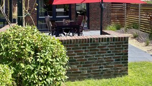 Een modern huis met een bakstenen gevel, een groot raam en een terras met een rode parasol.