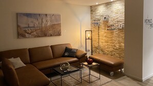Een moderne woonkamer met een bruine leren bank, een salontafel, een vloerlamp en een stenen muur met planken.