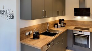 Een moderne keuken met grijze kastjes, een houten aanrecht, een waterkoker, een koffiezetapparaat en een inbouwoven.