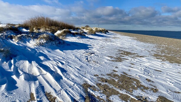 Een besneeuwd strand met duinen en een heldere lucht.