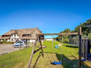 A house with a thatched roof, a swing set, and a car parked in the driveway.