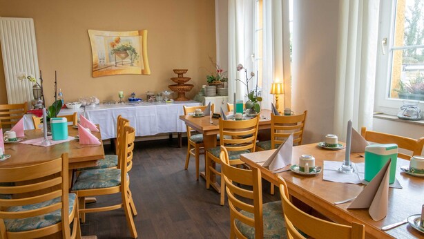 Spiseområde med træborde og stole, et hvidt borddække og et maleri på væggen.