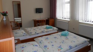Une chambre avec deux lits, un bureau, une chaise, une télévision et une fenêtre avec des rideaux.