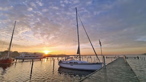 A marina with boats docked, a wooden pier, and a sunset in the background.