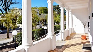 A covered outdoor area with white columns, a tiled floor, and a potted plant.