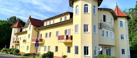 A yellow building with red roofs, multiple balconies, and a sign indicating a hotel.