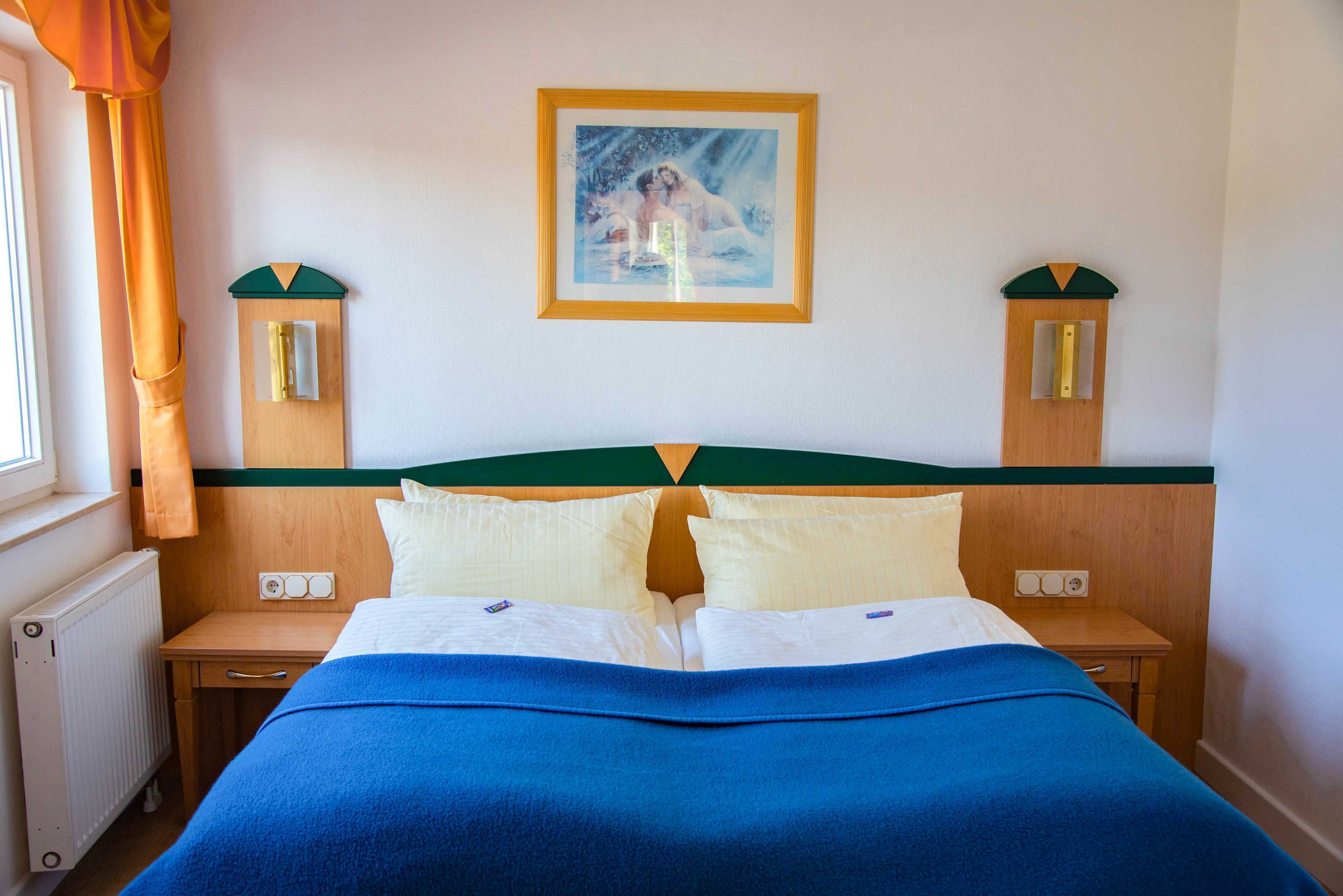 Une chambre d’hôtel avec un lit, deux tables de chevet, une commode, une fenêtre avec des rideaux et un tableau au mur.